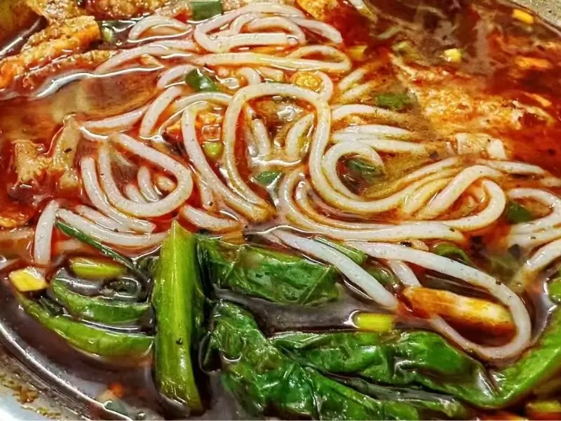Liuzhou rice noodles (Luosifen) with spicy broth, bamboo shoots, peanuts, and herbs.