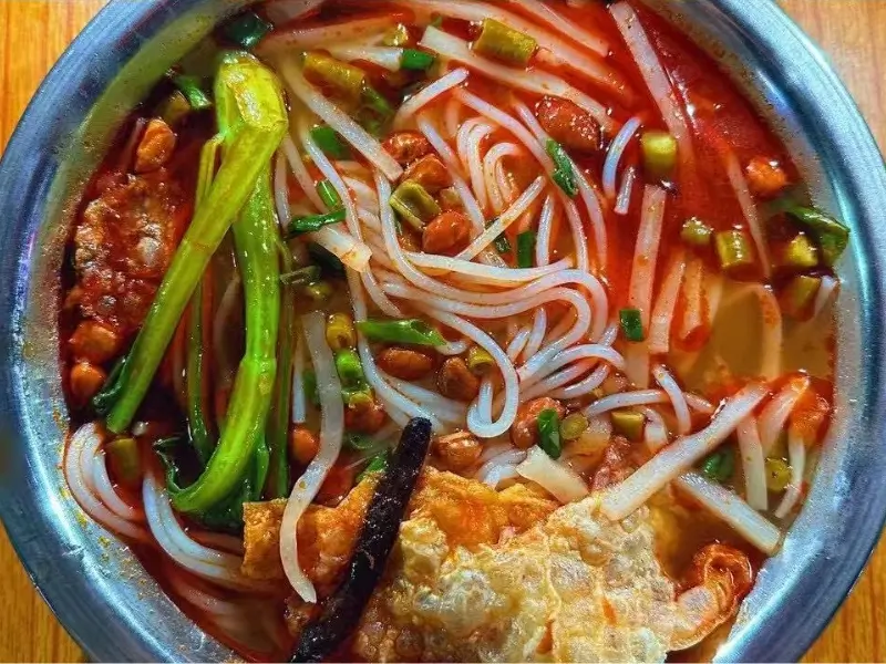 Liuzhou rice noodles (Luosifen) with spicy broth, bamboo shoots, peanuts, and herbs.
